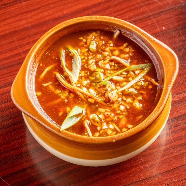A bowl of hot and sour soup with chopped vegetables and spices on a wooden table.