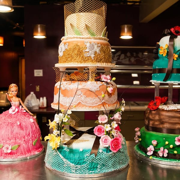 Several elaborately decorated, multi-tiered cakes, including a Barbie doll cake, displayed in a bakery.
