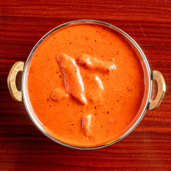 Overhead view of a metal bowl filled with orange butter chicken curry on a wooden table.