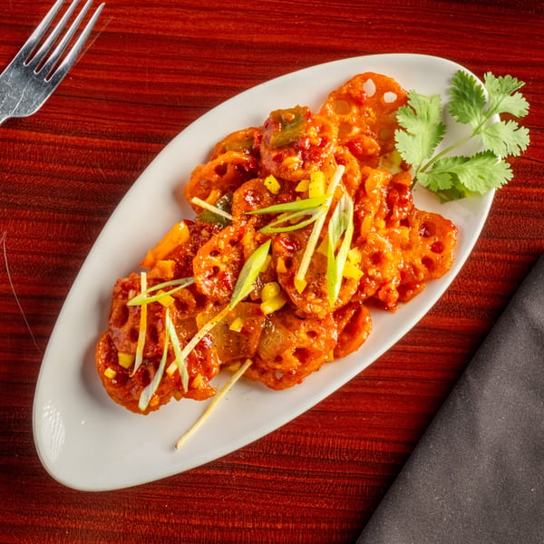 Spicy lotus root appetizer with green onions and cilantro on a white plate with a fork and napkin.