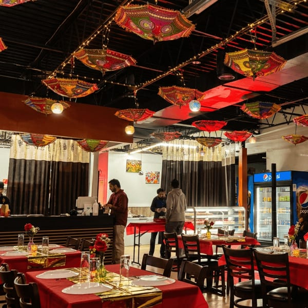 Vibrant restaurant interior with colorful hanging umbrellas, red tablecloths, and staff behind a counter.