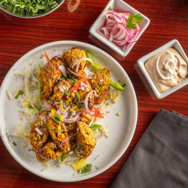 Chicken tikka with chopped onions, bell peppers, and cilantro, served with sauces and a fork.